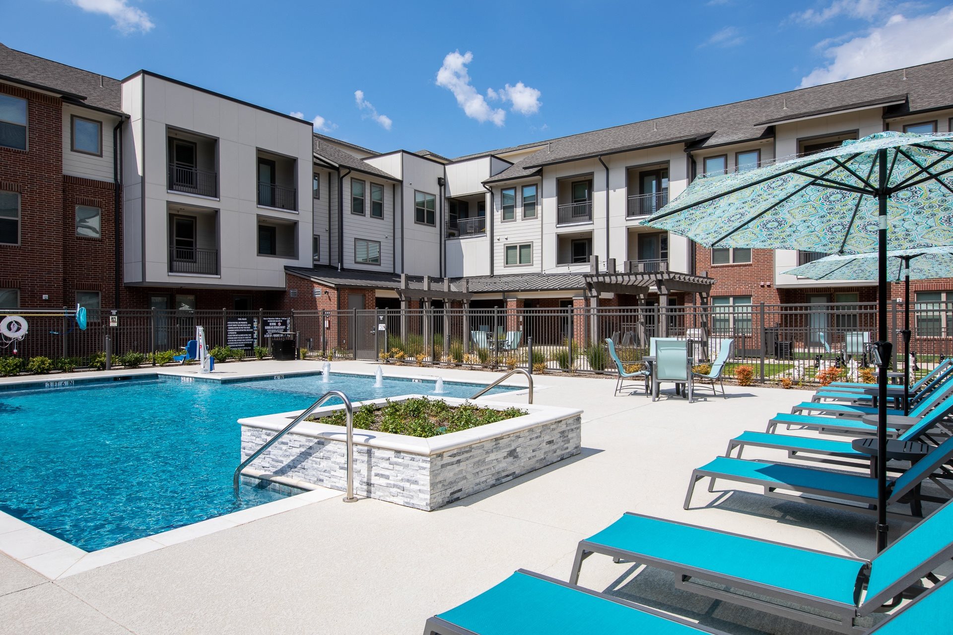 a resort-style swimming pool with lounge chairs and a firepit at a senior apartment community